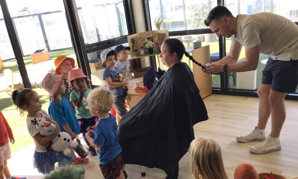 Children watching as a man plaits Jo's hair ready for shaving to support World's Greatest Shave