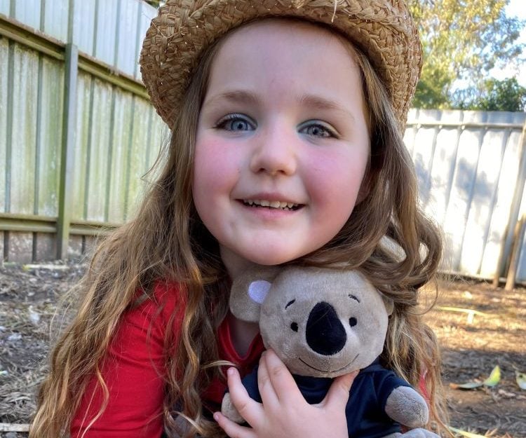 A young girl wearing a hat and holding a Koala toy